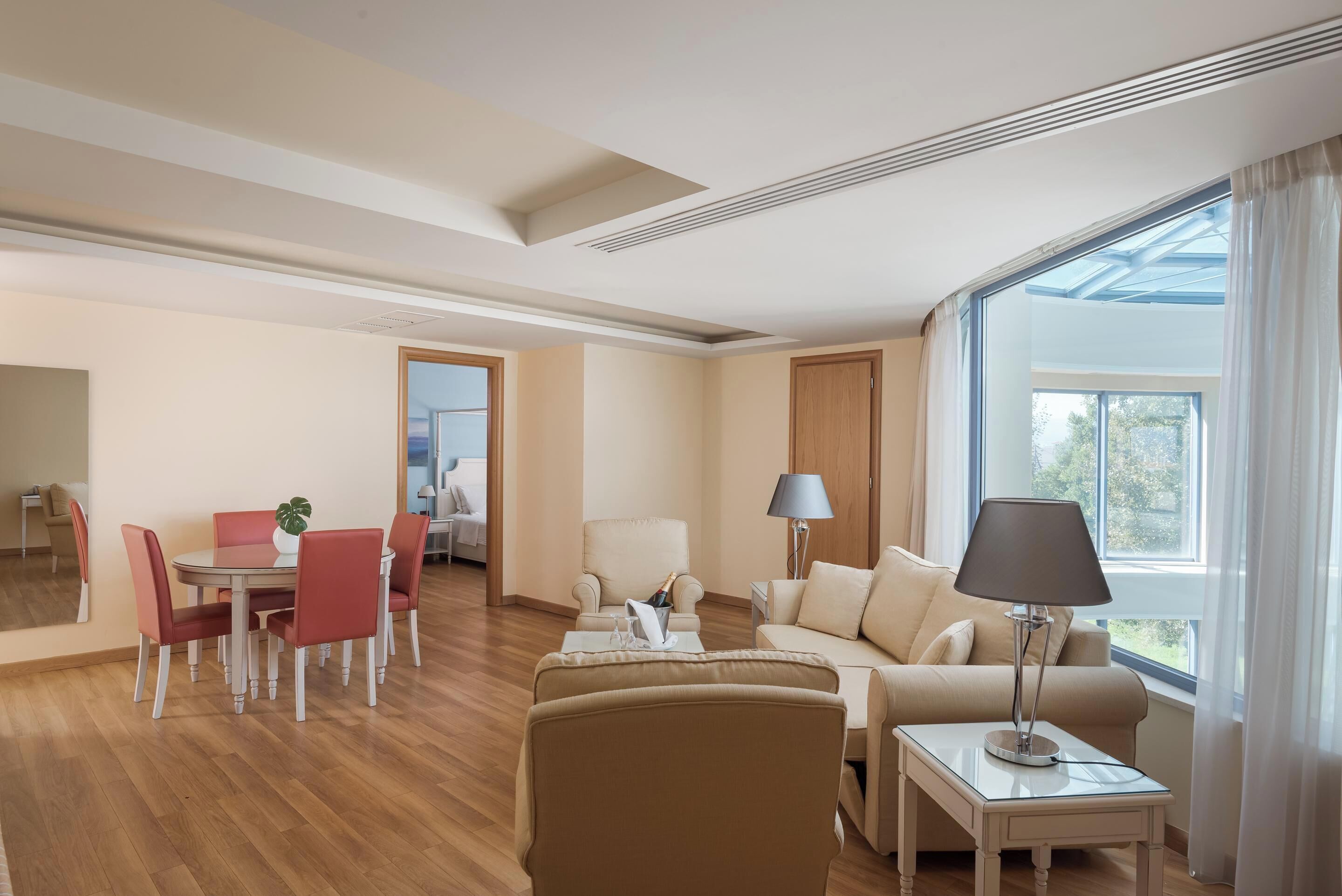 Ein modernes Hotelzimmer mit Essbereich, einer Couch, einer Lampe und großen Fenstern.