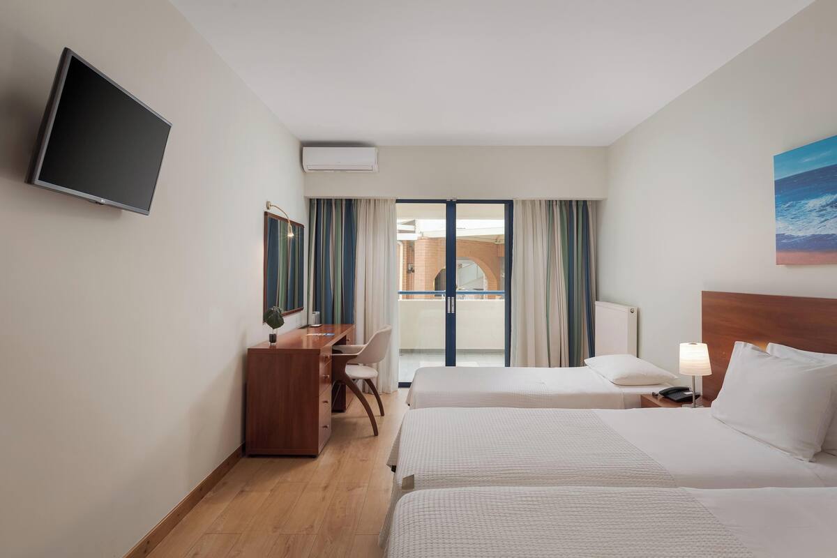 A hotel room with two beds, a desk, a chair, a TV, and a window with curtains.