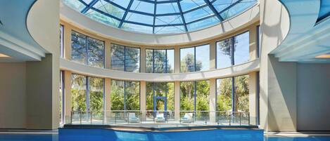 A large indoor swimming pool with a glass ceiling and multiple levels of seating.