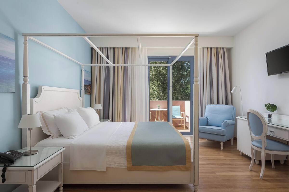 A bedroom with a four-poster bed, a desk with a chair, and a TV mounted on the wall.