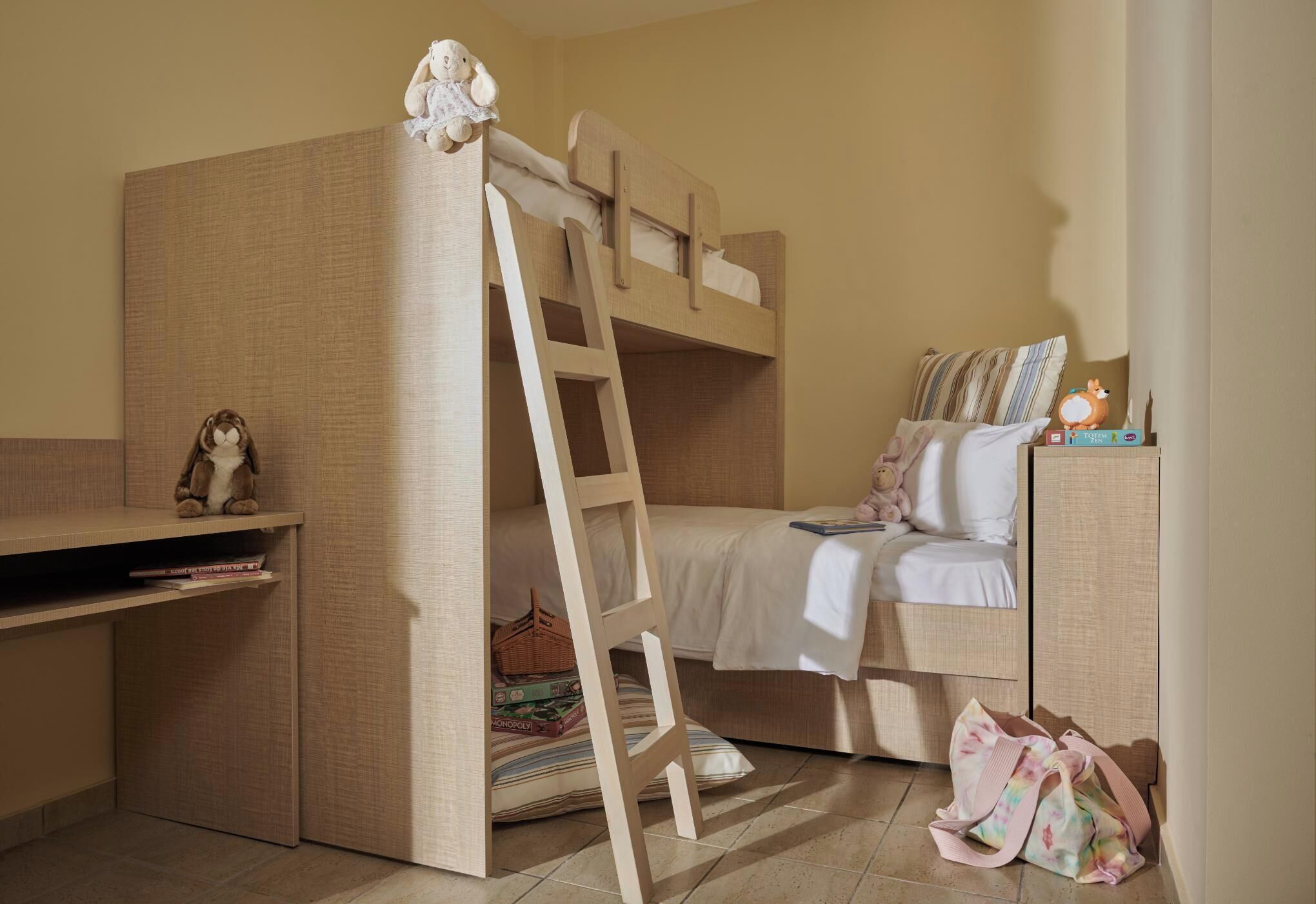 Una cama litera con una escalera, un escritorio con un peluche y una pequeña estantería con libros.