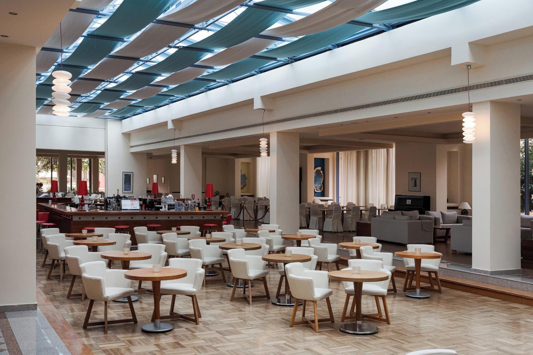 A spacious indoor area with multiple seating arrangements, including round tables and chairs, and a bar area with a counter and bar stools.