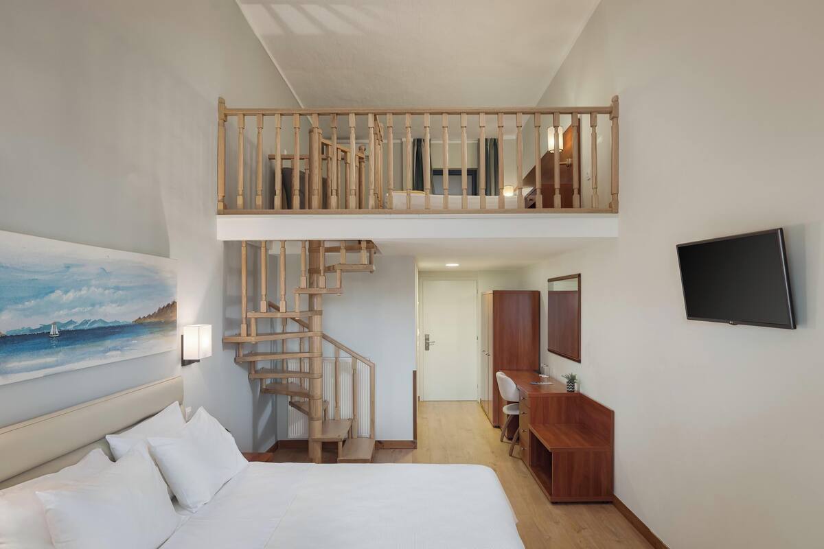 A hotel room with a bed, a desk, a TV, a painting, and a staircase to an upper level.