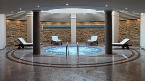 A spa area with a hot tub, lounge chairs, and a stone wall. - Alkyon Resort Hotel & Spa (Velo-Vocha)