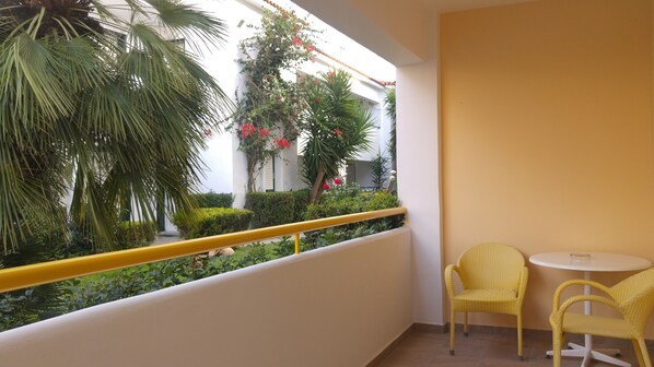 A balcony with yellow chairs, a yellow railing, and a view of a garden with palm trees and red flowers. - Alkyon Resort Hotel & Spa (Velo-Vocha)
