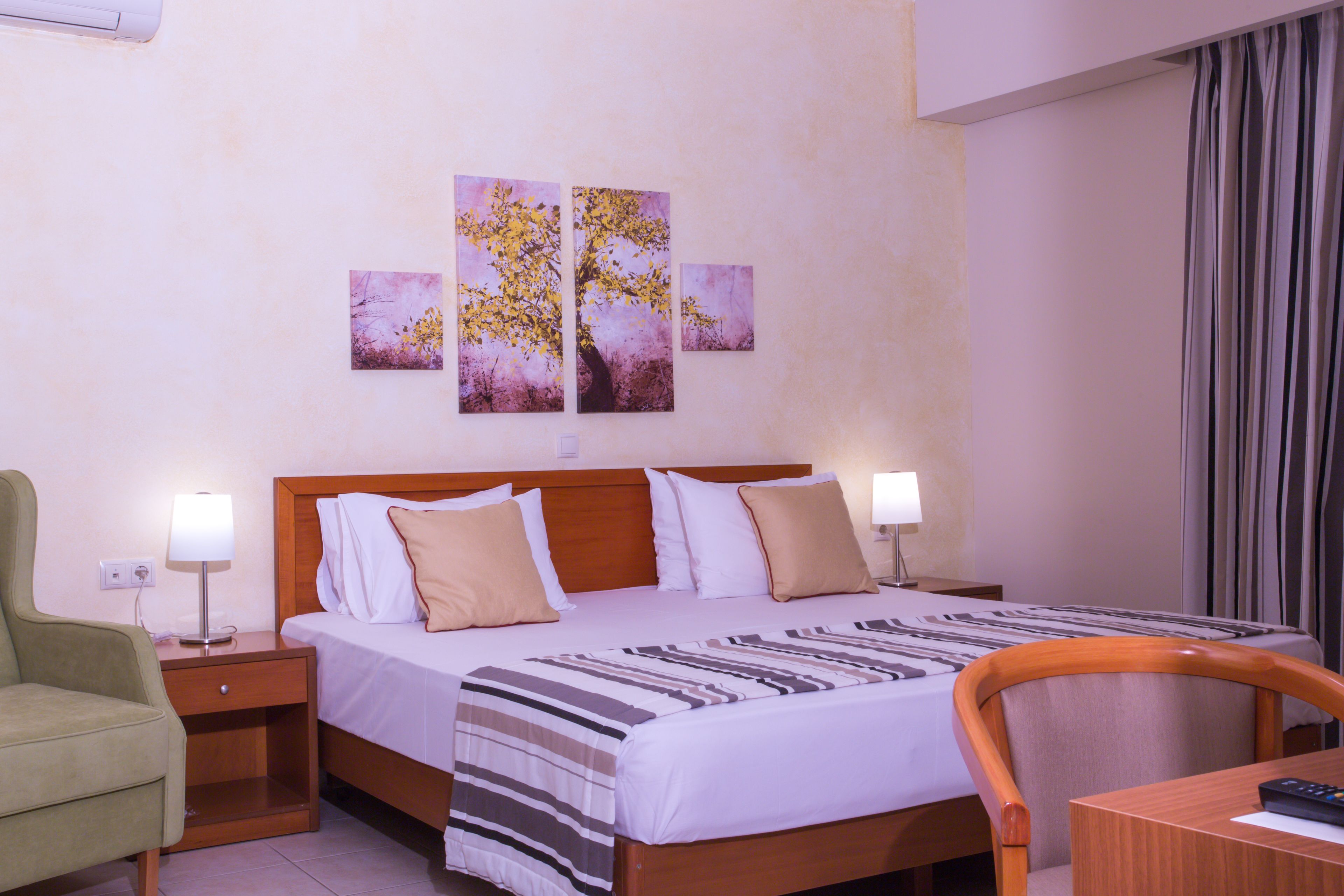 A hotel room with a bed, two bedside tables, a chair, a desk, and a wall with three paintings.