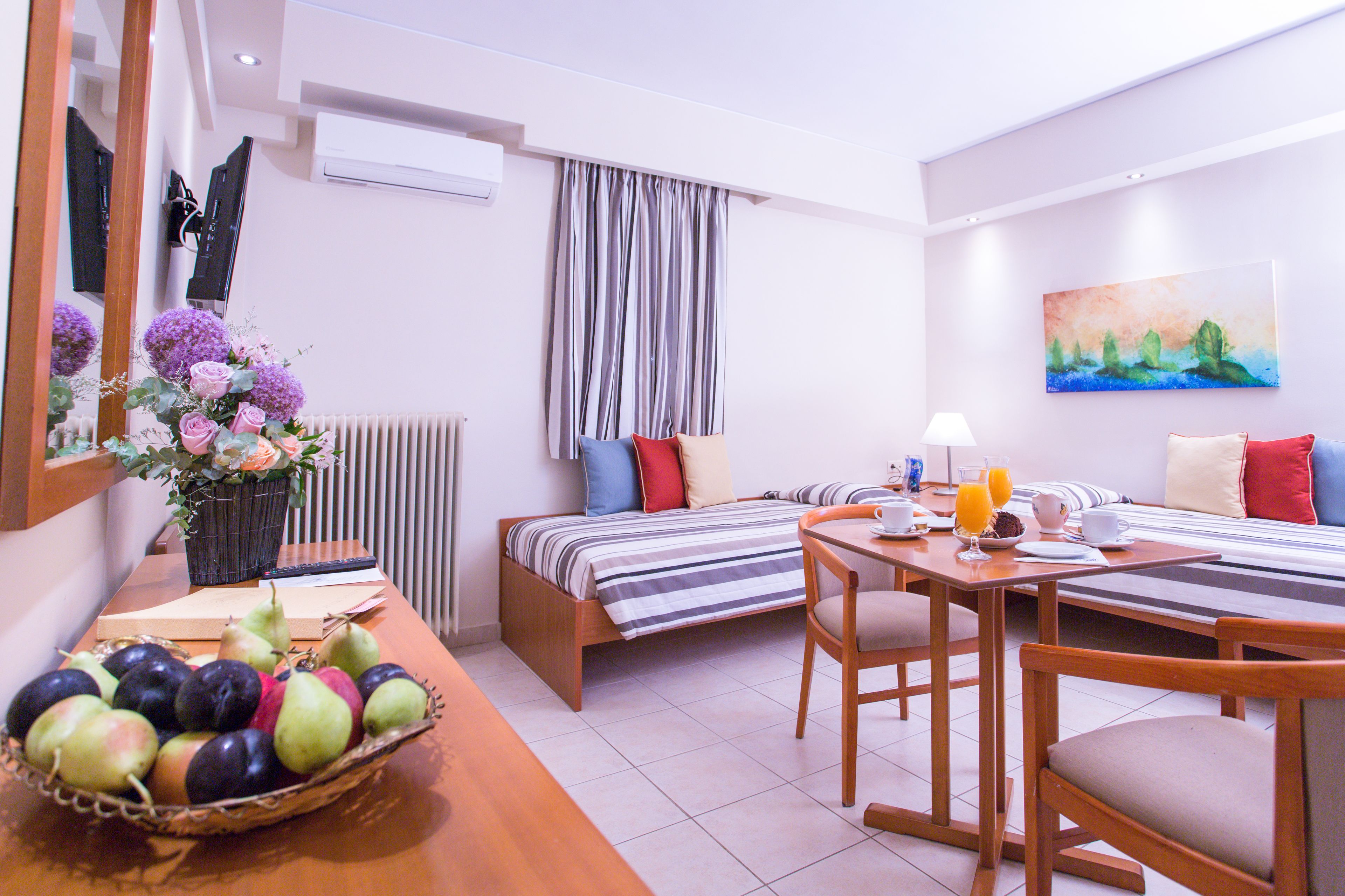 Ein Hotelzimmer mit einem Bett, einem Esstisch mit Stühlen, einer Obstschale und einem Gemälde an der Wand.