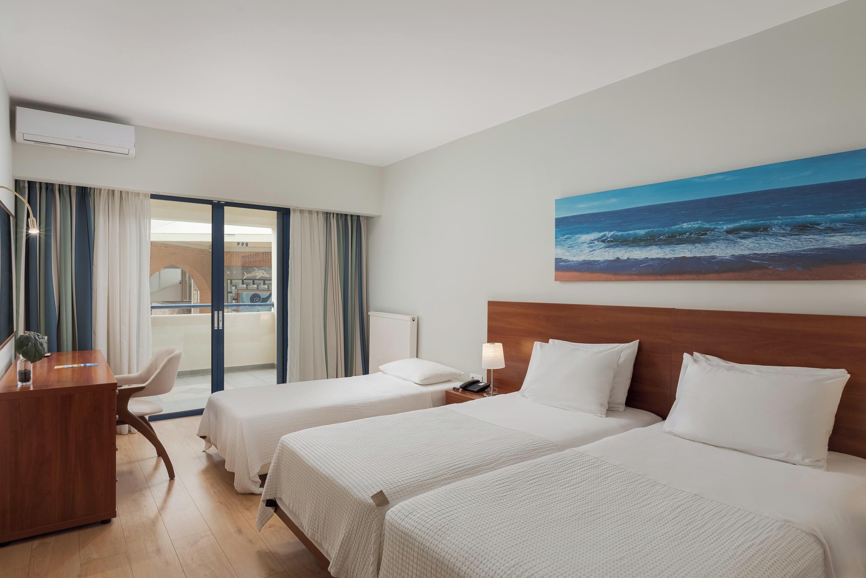 Une chambre d’hôtel avec deux lits, un bureau, une chaise et un tableau représentant l’océan.