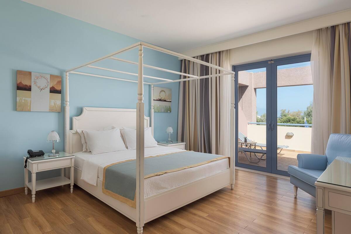 A bedroom with a four-poster bed, a nightstand with a lamp, and a view of the outdoor patio.