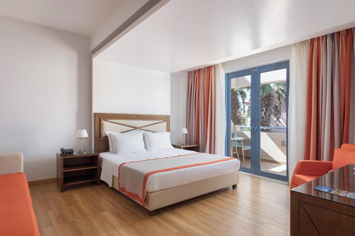 A hotel room with a bed, bedside table, lamp, and a view of the outdoors through a sliding glass door.