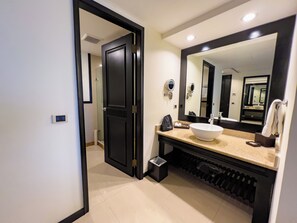 Un baño moderno con un espejo grande, un lavamanos blanco y una puerta negra.