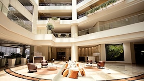 A spacious lobby with a central seating area, multiple floors, and a large window providing a view of the outdoors.