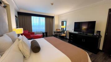 Une chambre d’hôtel avec un grand lit, un bureau avec un ordinateur, une télévision et un fauteuil rouge.