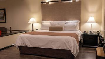 Quarto de hotel com cama grande, duas luminárias de cabeceira, mesa de cabeceira, escrivaninha e uma cadeira.