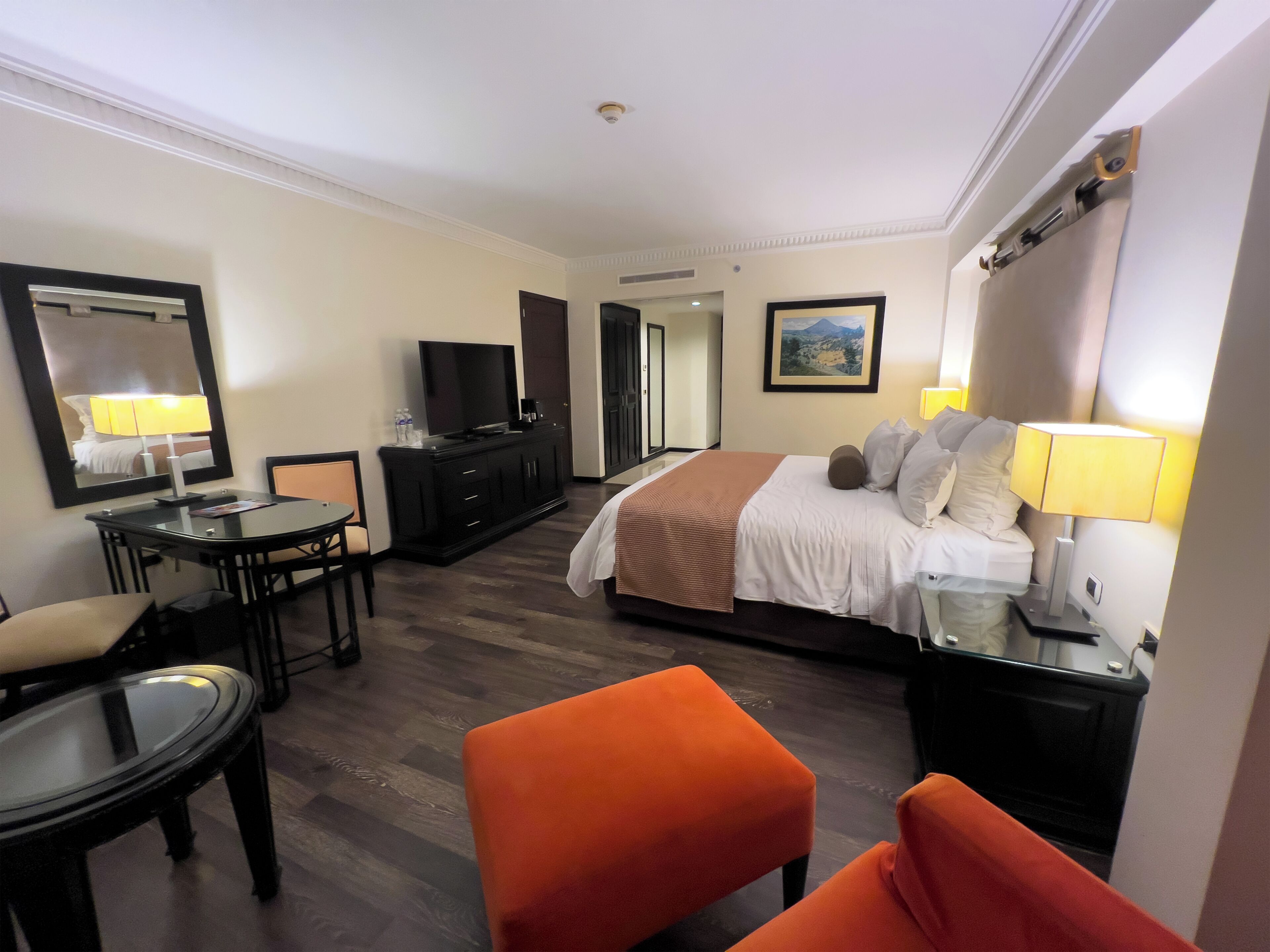 A hotel room with a bed, a desk, a chair, a television, and a painting on the wall.