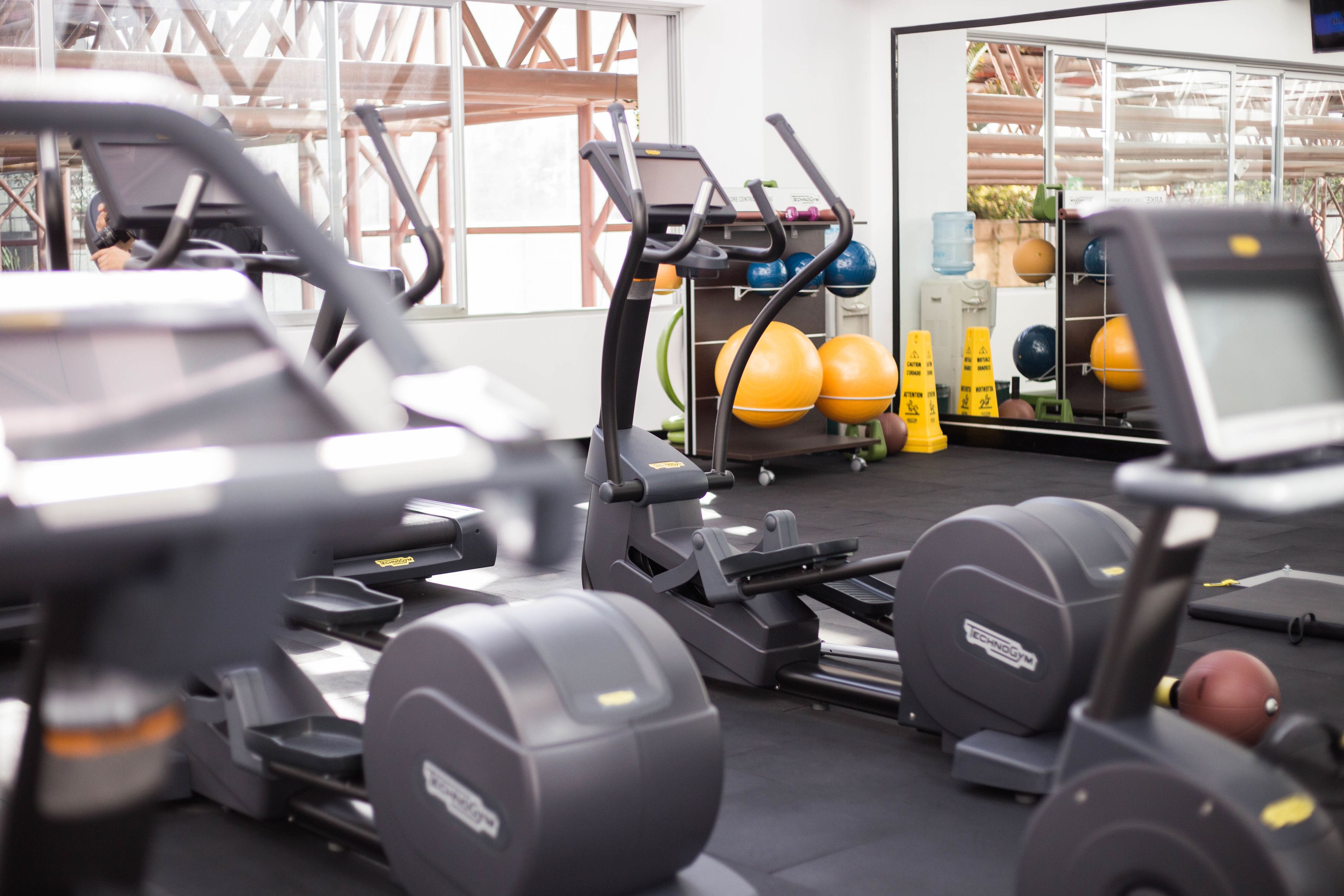 Un gimnasio con equipo de ejercicio, incluyendo cintas de correr y máquinas de pesas, además de un estante con balones de ejercicio.