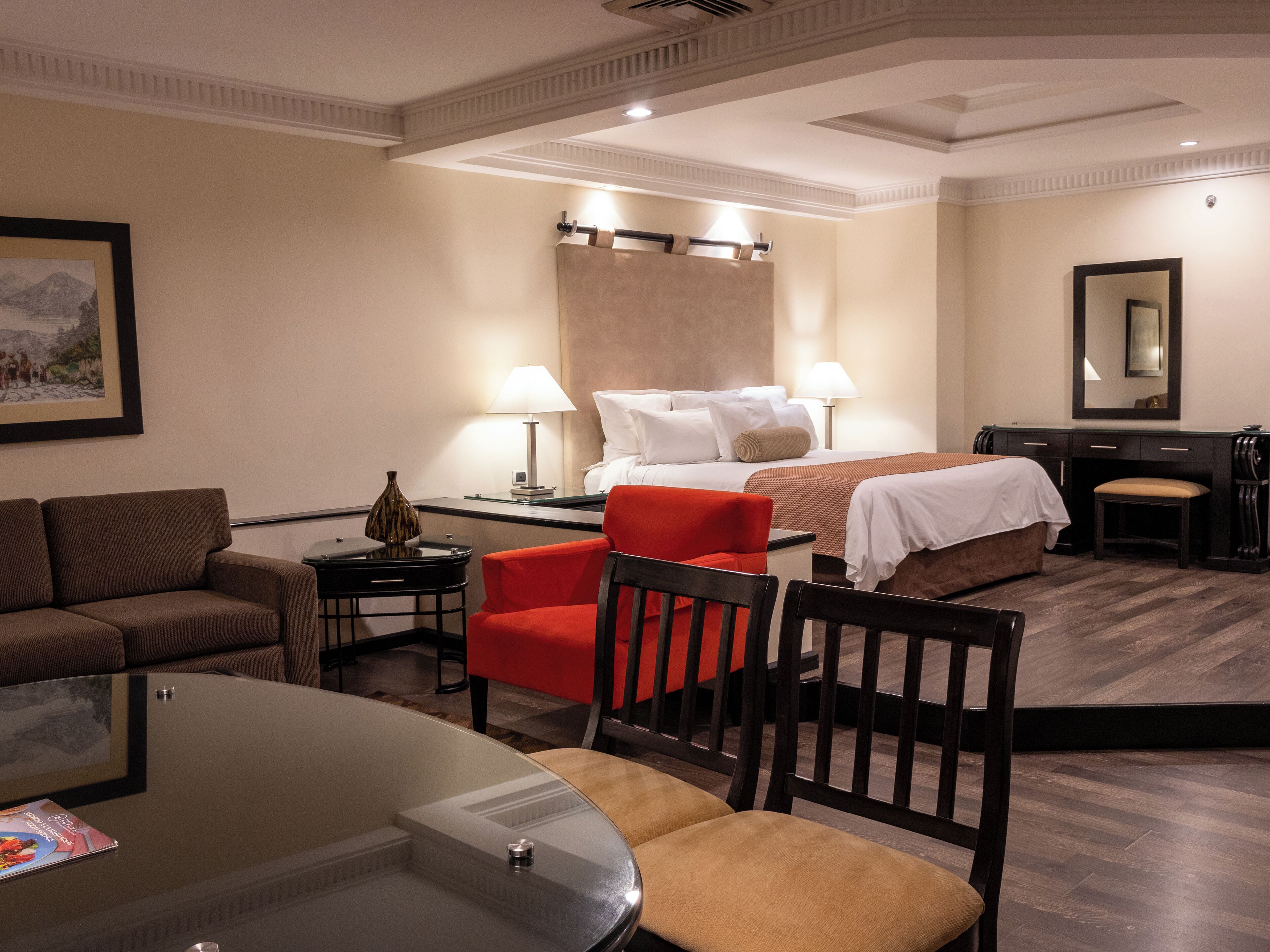 Quarto de hotel com cama, secretária, cadeira, sofá e mesa de jantar.