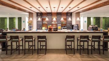 A bar area with wooden chairs, a central counter with a fruit display, and hanging pendant lights.