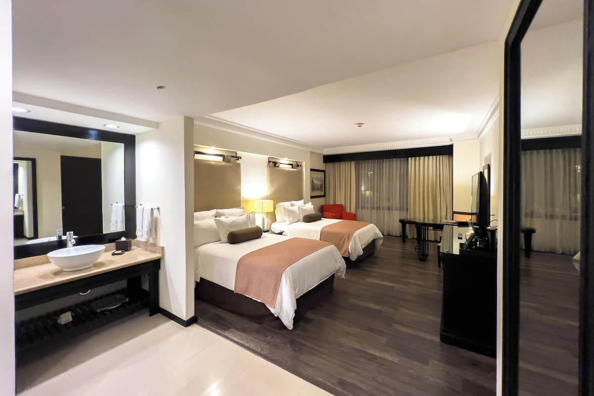 Habitación de hotel con dos camas, un espejo grande, un lavamanos y una mesita pequeña.