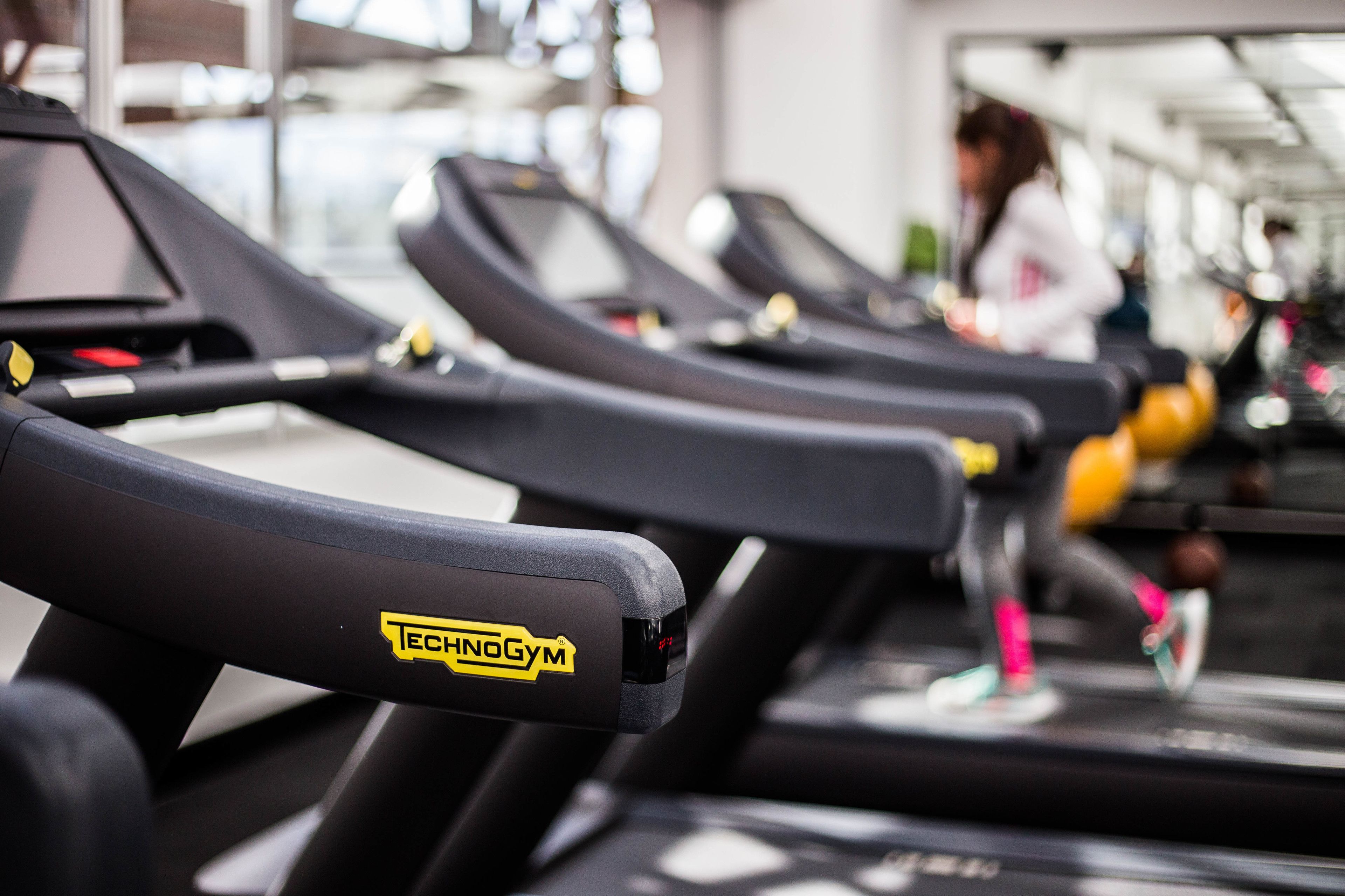 Une rangée de tapis de course dans une salle de sport, avec le nom de la marque bien visible.
