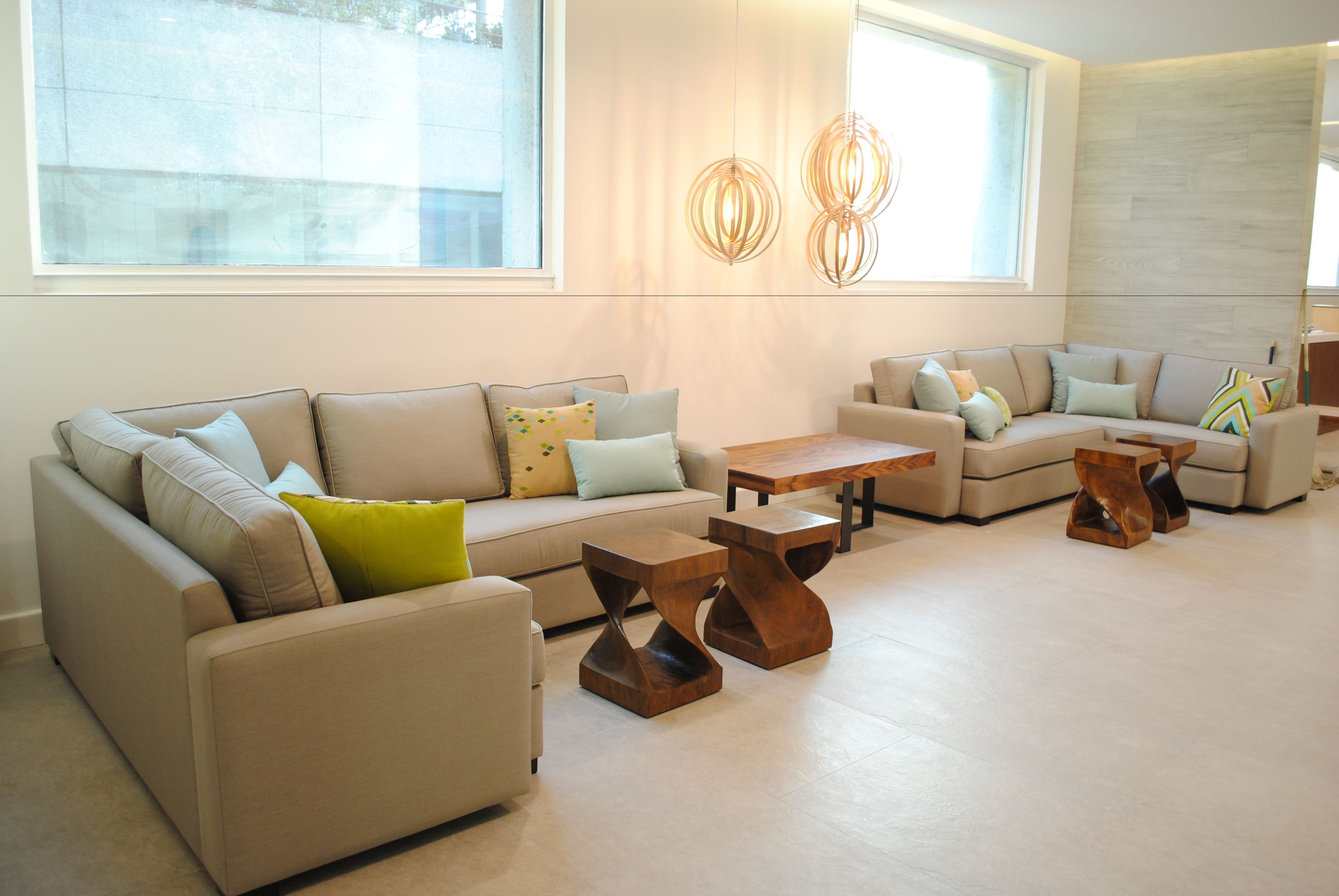 A modern living room with a beige sofa set, wooden coffee tables, and a large window providing natural light.