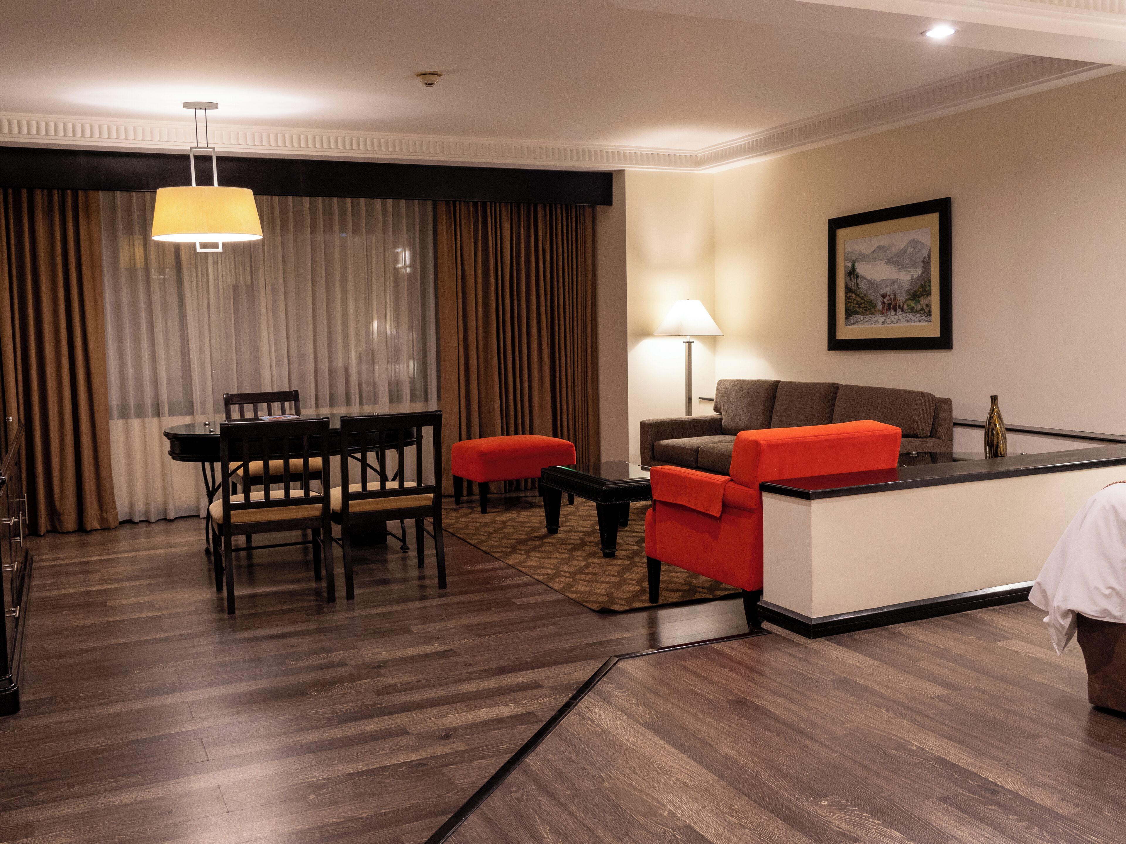 A hotel room with a dining area, a sofa, a lamp, and a painting on the wall.