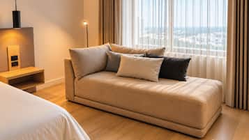 Quarto de hotel moderno com sofá-cama, mesa de cabeceira, abajur e vista da cidade através de amplas janelas.