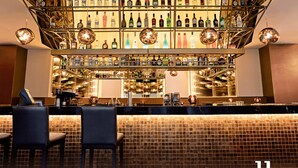 A bar area with multiple shelves of bottles, two bar stools, and a tiled backsplash.