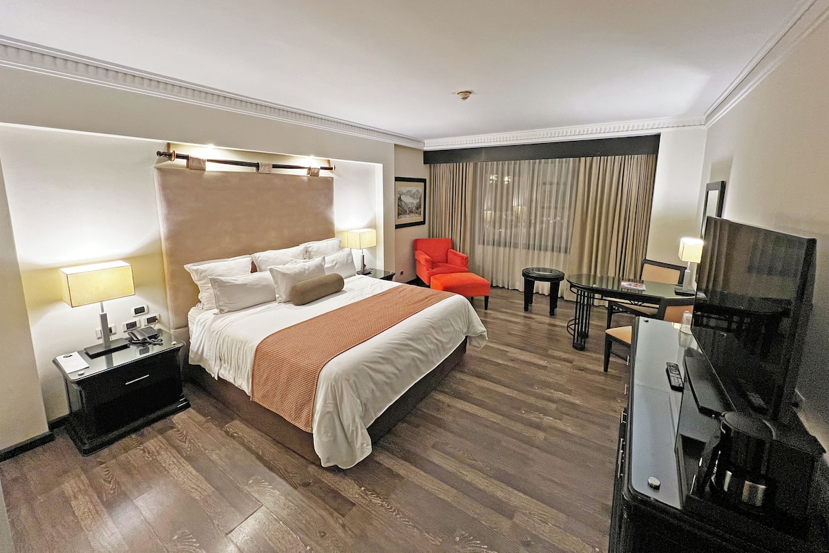 Una habitación de hotel con una cama grande, un escritorio, una silla, un televisor y una mesita.