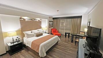Una habitación de hotel con una cama grande, un escritorio, una silla, un televisor y una mesita.