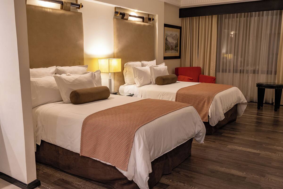 Habitación de hotel con dos camas, una silla roja, una lámpara y un cuadro en la pared.