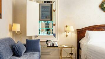 A hotel room with a bed, a sofa, a small table with a lamp, and a mirror reflecting the room.