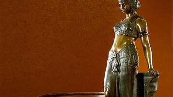 Uma estátua em um pedestal, num quarto com um sofá ornamentado e uma mesa.