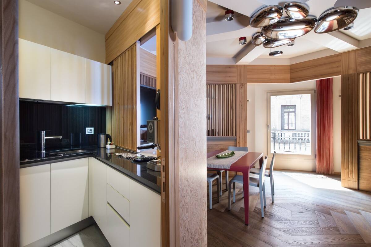 Une cuisine moderne avec des meubles blancs, un plan de travail noir et un coin repas comprenant une table et des chaises.