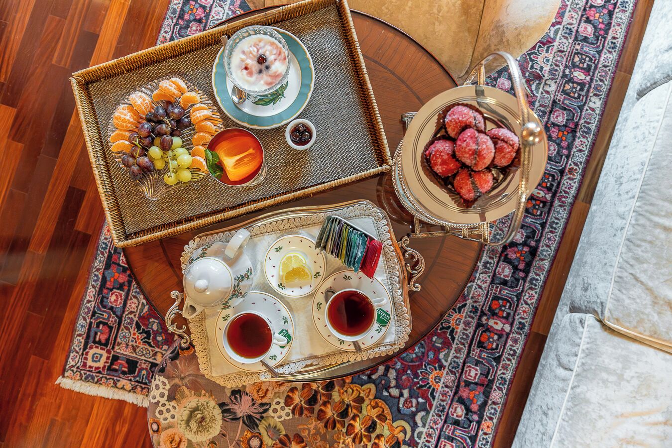 A tray with fruits, a glass of yogurt with berries, and a teapot with cups on a patterned rug.