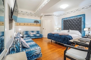 Ein Schlafzimmer mit Bett, Sofa, Sessel, Schreibtisch und Fernseher.