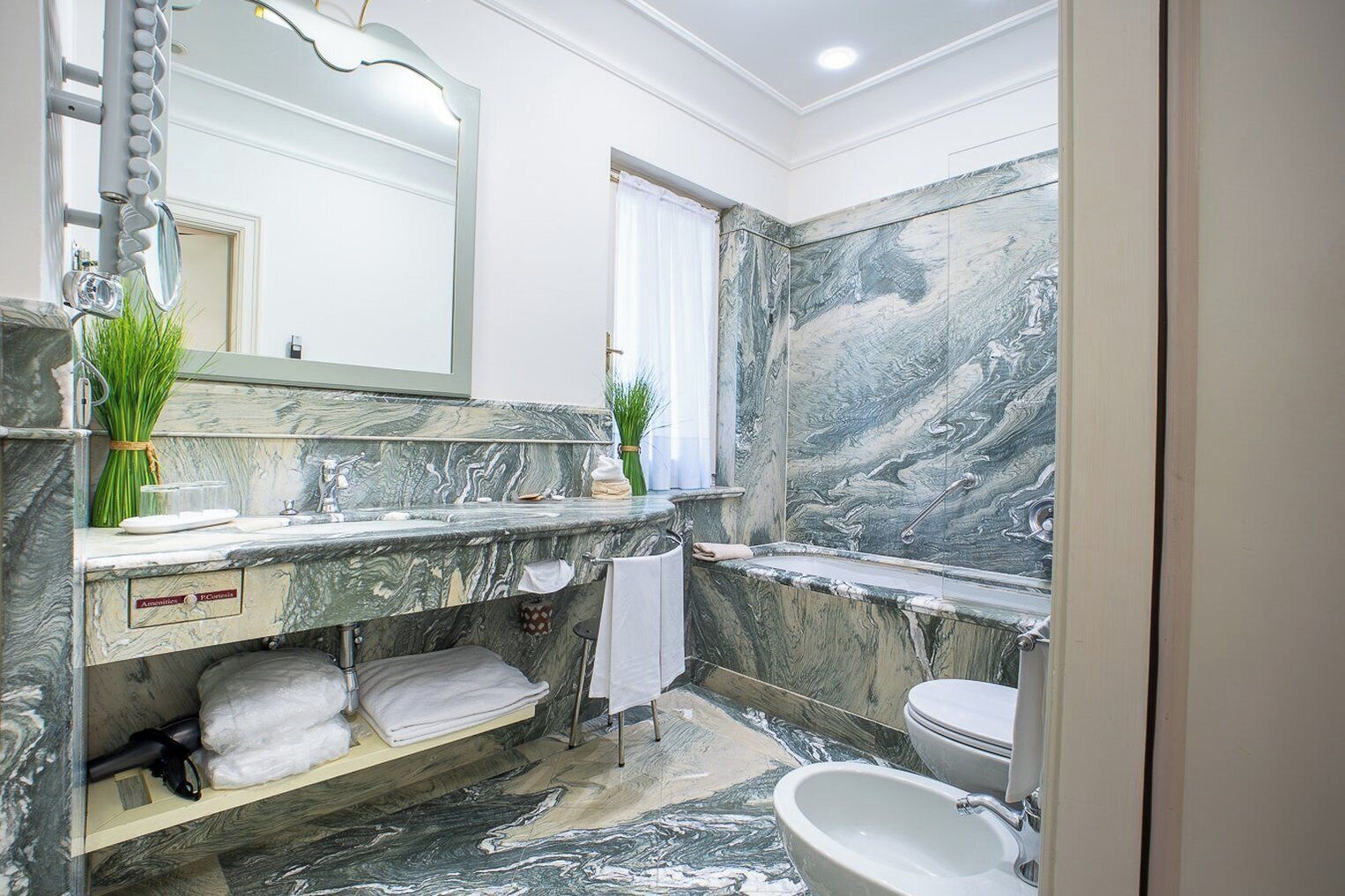 Un bagno con un vanità in marmo, un grande specchio, un water e una zona doccia.