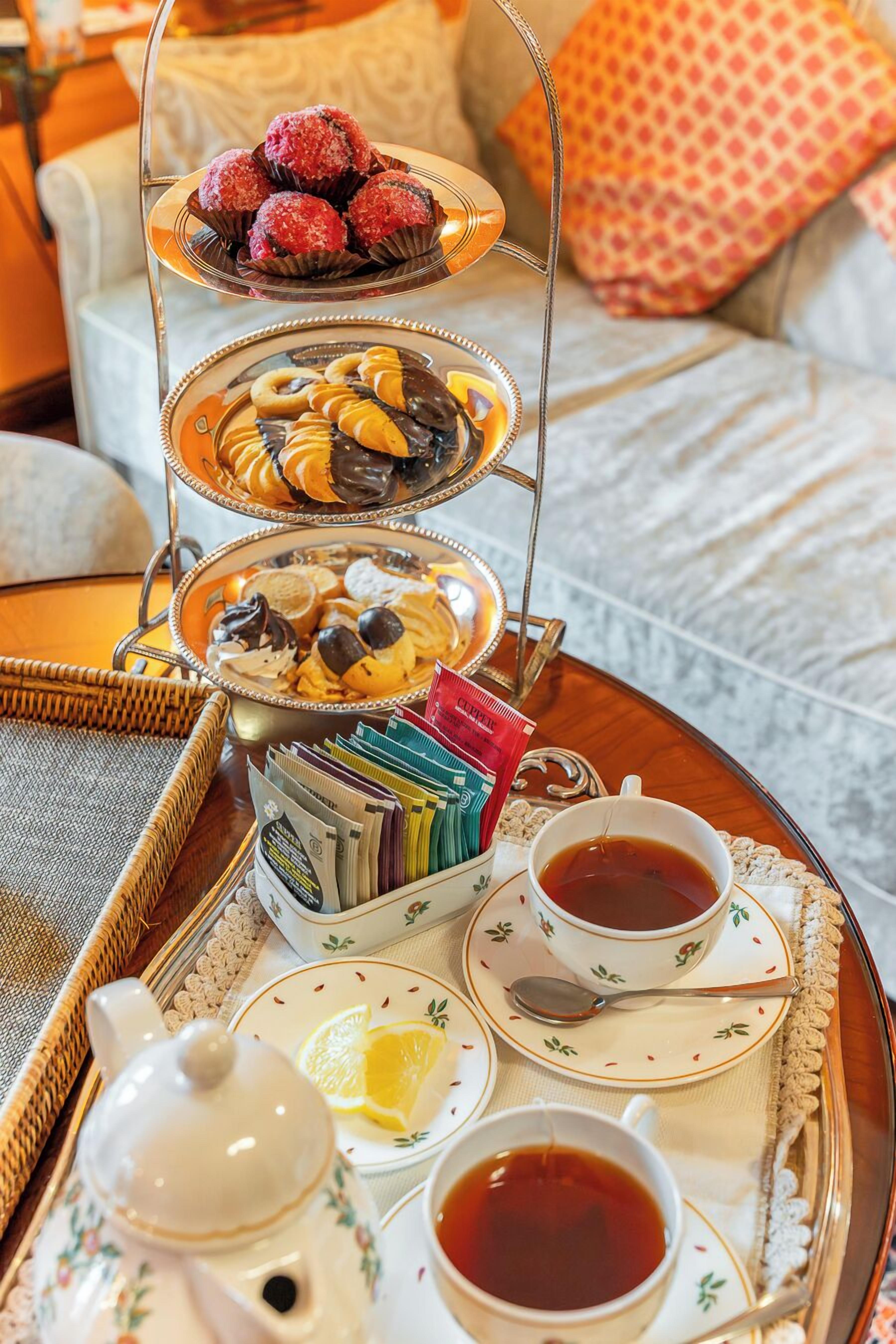 Una bandeja con té, una tetera y un frutero escalonado con pasteles y bombones.