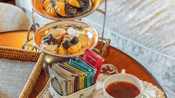 Una bandeja con té, una tetera y un frutero escalonado con pasteles y bombones.