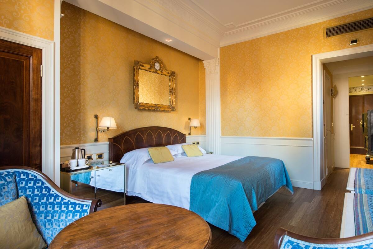 Une chambre d’hôtel avec un grand lit, deux tables de chevet, un miroir et une petite table ronde.