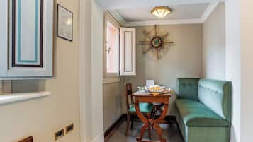 Un pasillo estrecho con un sofá verde, una silla de madera, una mesa con papeles y una taza, un reloj de pared y un cuadro enmarcado.