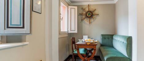 A narrow hallway with a green sofa, a wooden chair, a table with papers and a cup, a wall clock, and a framed picture.