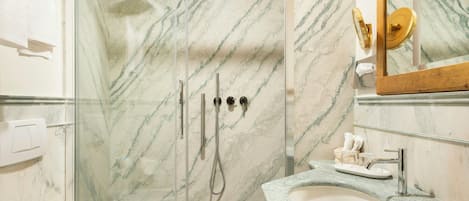 A bathroom with a glass shower enclosure, a sink with a marble countertop, and a mirror with a gold frame.