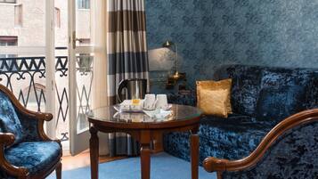 A room with a blue patterned wall, a blue sofa, a wooden coffee table, two blue armchairs, a striped curtain, and a view of a building through a glass door.