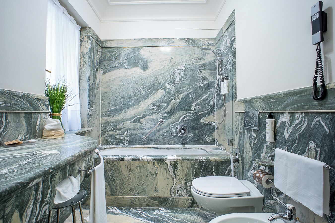 A bathroom with a marble wall, a bathtub, a toilet, and a sink.