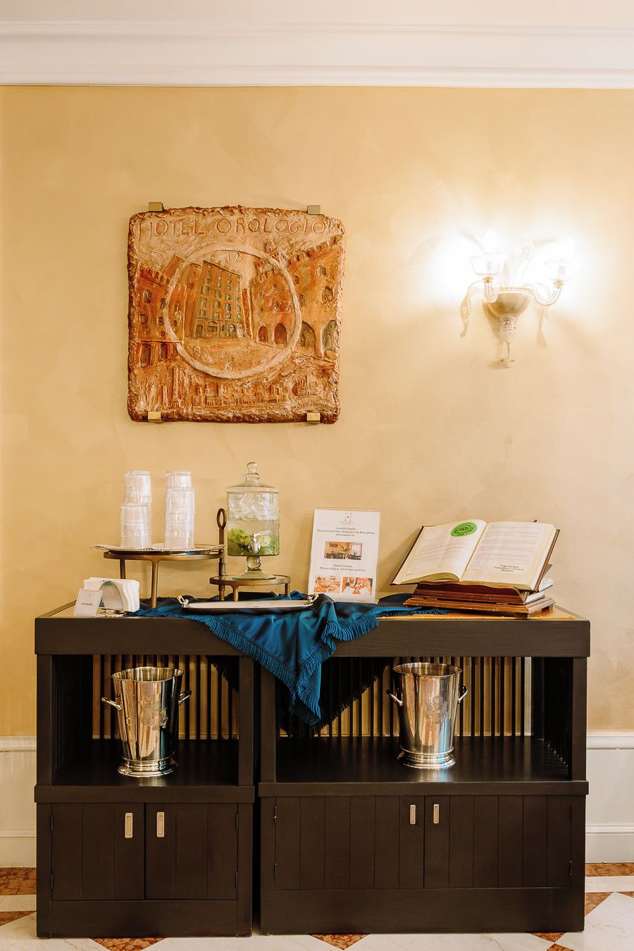 A reception desk with a vintage wall art, a sign, and a book. There are two metal containers on the desk.