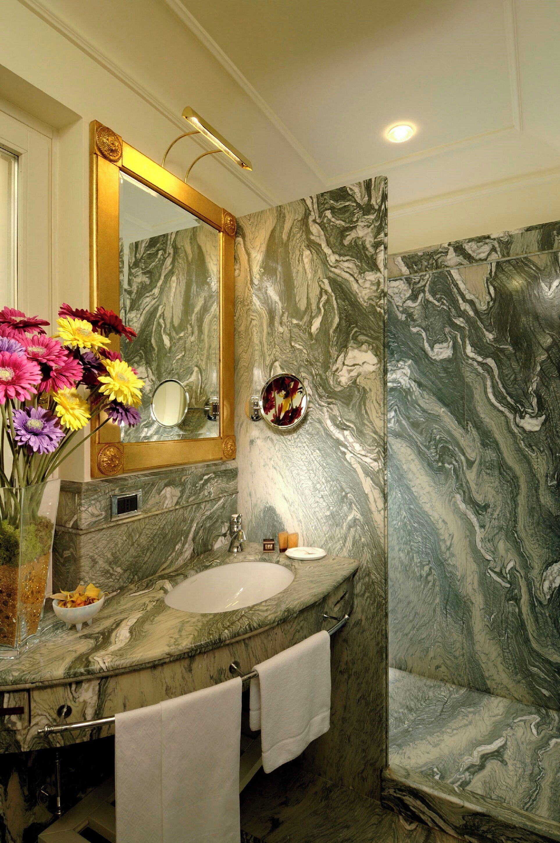 A bathroom with a marble sink, a large mirror, and a vase of flowers.