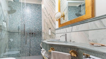 Un baño con ducha envuelta en vidrio, un lavamanos de mármol y un espejo con marco dorado.