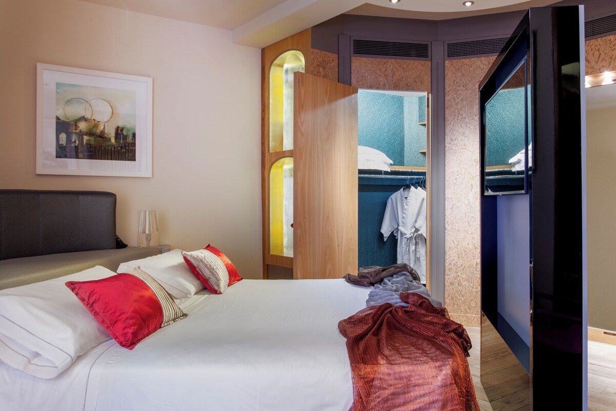 Une chambre d’hôtel moderne avec un grand lit, une armoire, un miroir et une œuvre d’art encadrée au mur.
