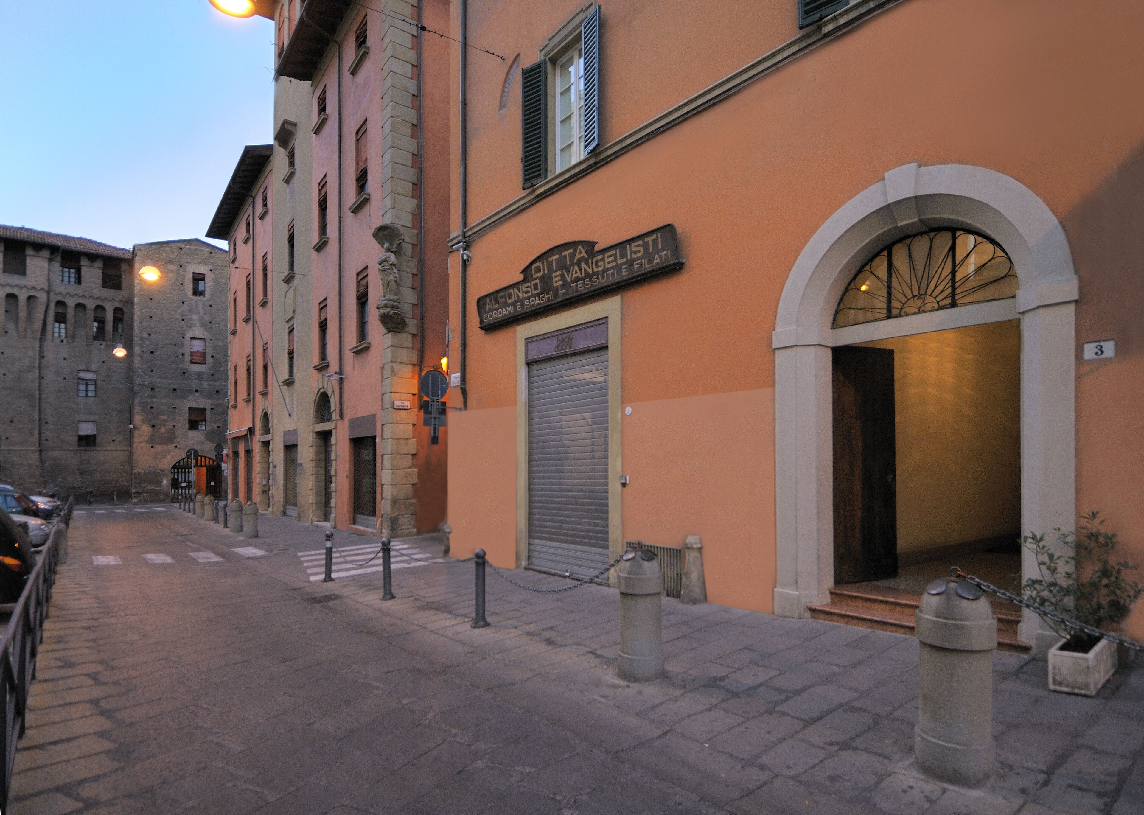 A street view with a building featuring a closed shutter and a sign with Italian text.